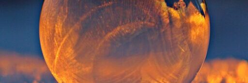 Close-up shot of a frozen bubble with warm reflections resting on a snowy surface at twilight.
